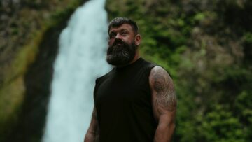 a man with a beard standing in front of a waterfall