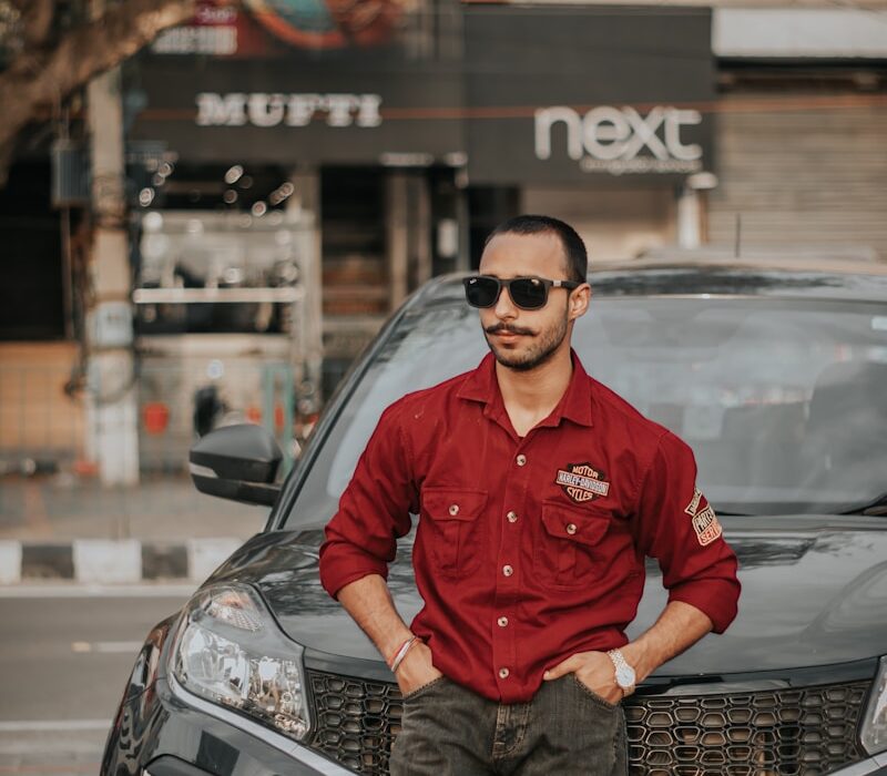 man in red long sleeve shirt and blue denim jeans sitting on black car